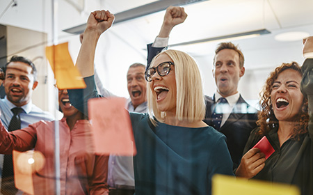 Jubelnde Personen vor einem Glas-Board mit Post-Its